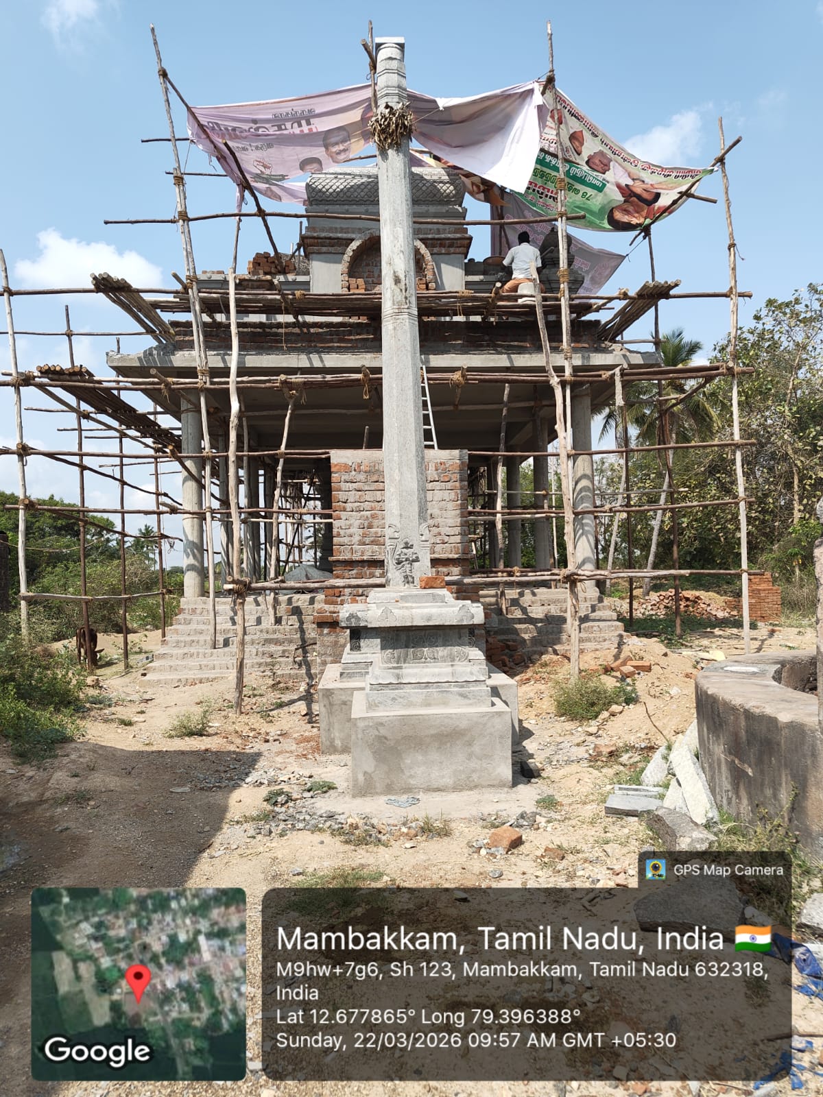 The new temple at Mambakkam under construction — stone pillar in the foreground, bamboo scaffolding around the gopuram